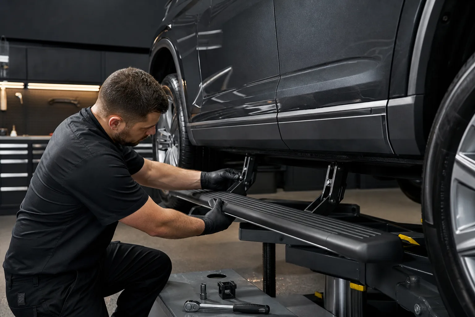 A technician aligning a black running board beneath a dark SUV in a professional workshop